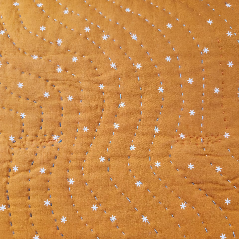 Close up photo of the back of Spin Me to Sleep, showing deep yellow fabric and Sarah’s curved lines of hand stitching.