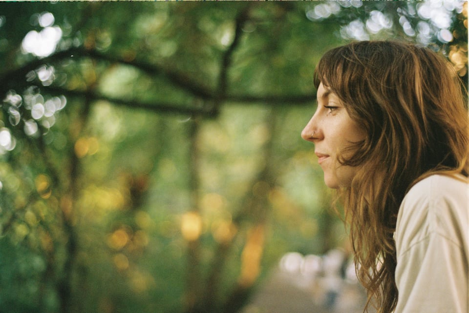 A woman with long honeyed hair wearing a white shirt is shown in profile, facing to the left.