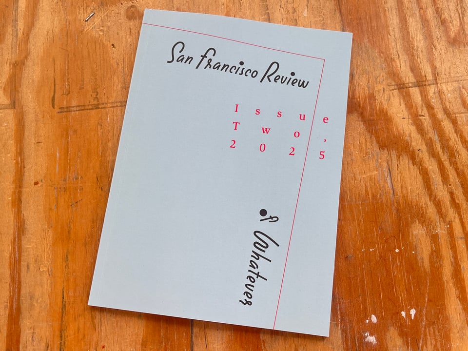 A photograph of Issue Two. It's a grayish blue magazine with black handpainted text that reads San Francisco Review of Whatever, and in red type Issue Two, 2025. There is an angled red line.