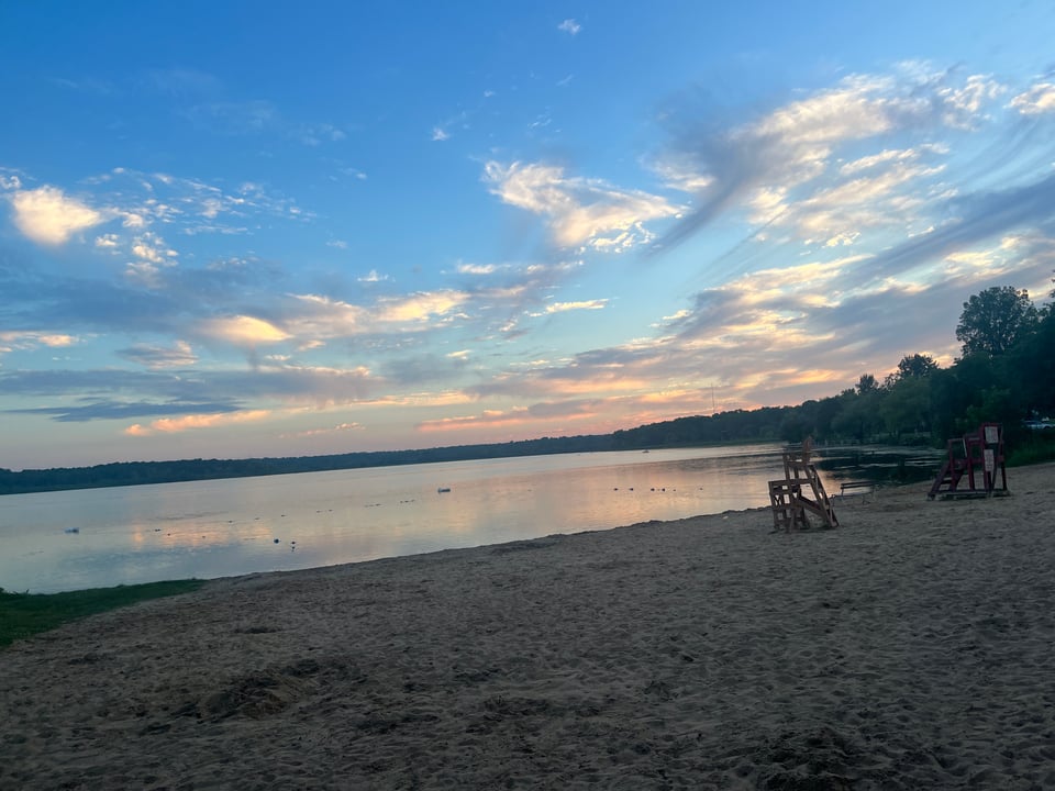 Wingra Beach at sunset with wispy clouds and pale pink and gold reflections in the water