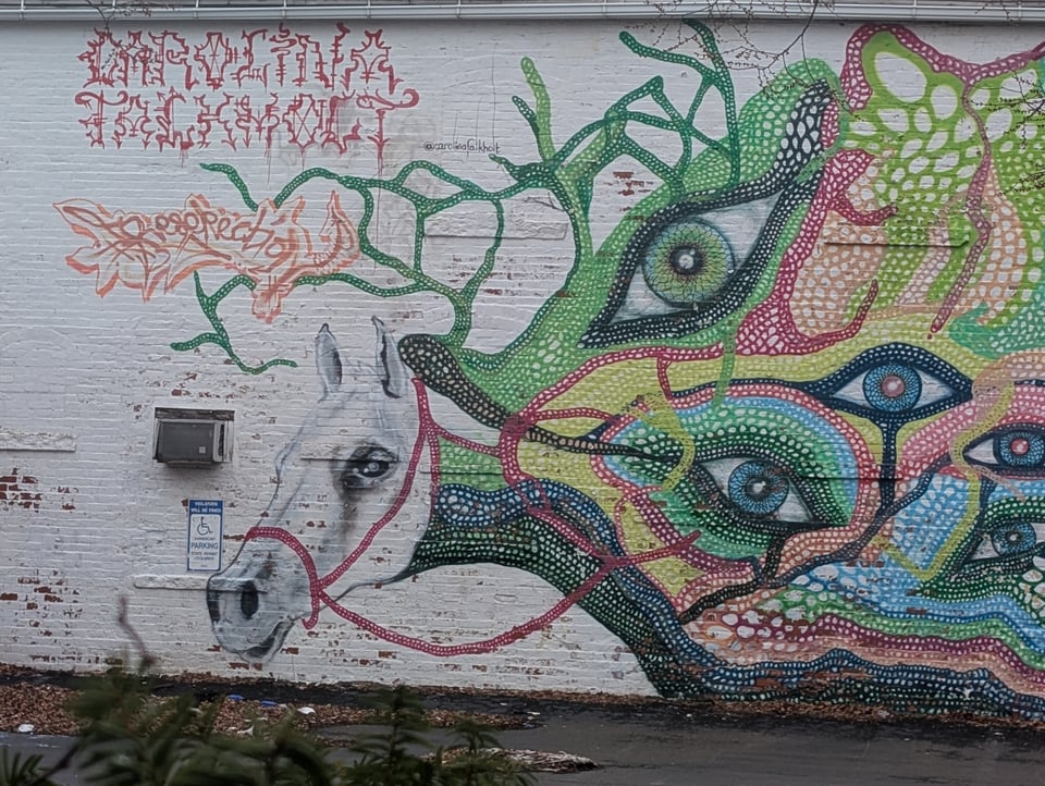 Street art shows a white horse head emerging from a weird blobby creature with a lot of eyes and multicolored fibers