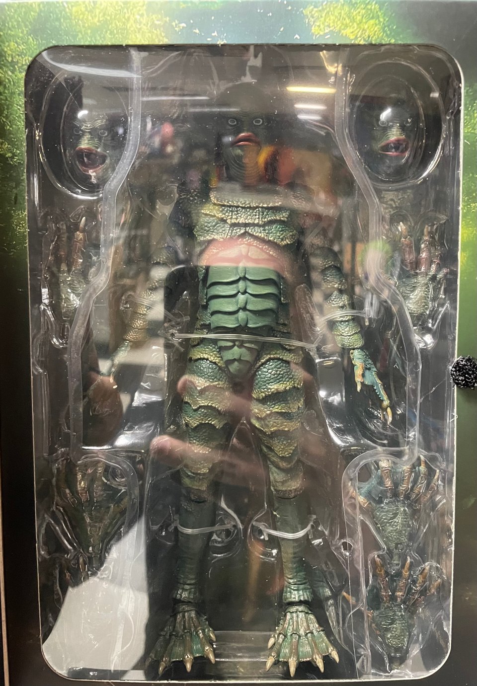 A large toy in a box of the Creature From The Black Lagoon with multiple heads and different expressions