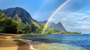 A sunny beach in Hawaii with a rainbow over it.