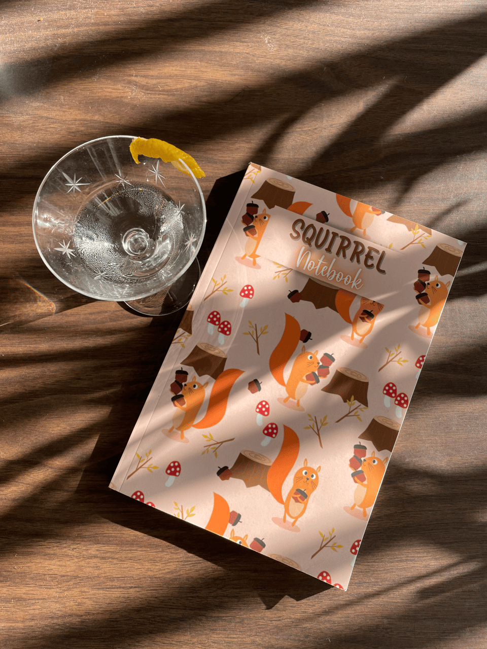A small martini in a starburst cocktail glass next to a notebook full of pictures of cartoon squirrels