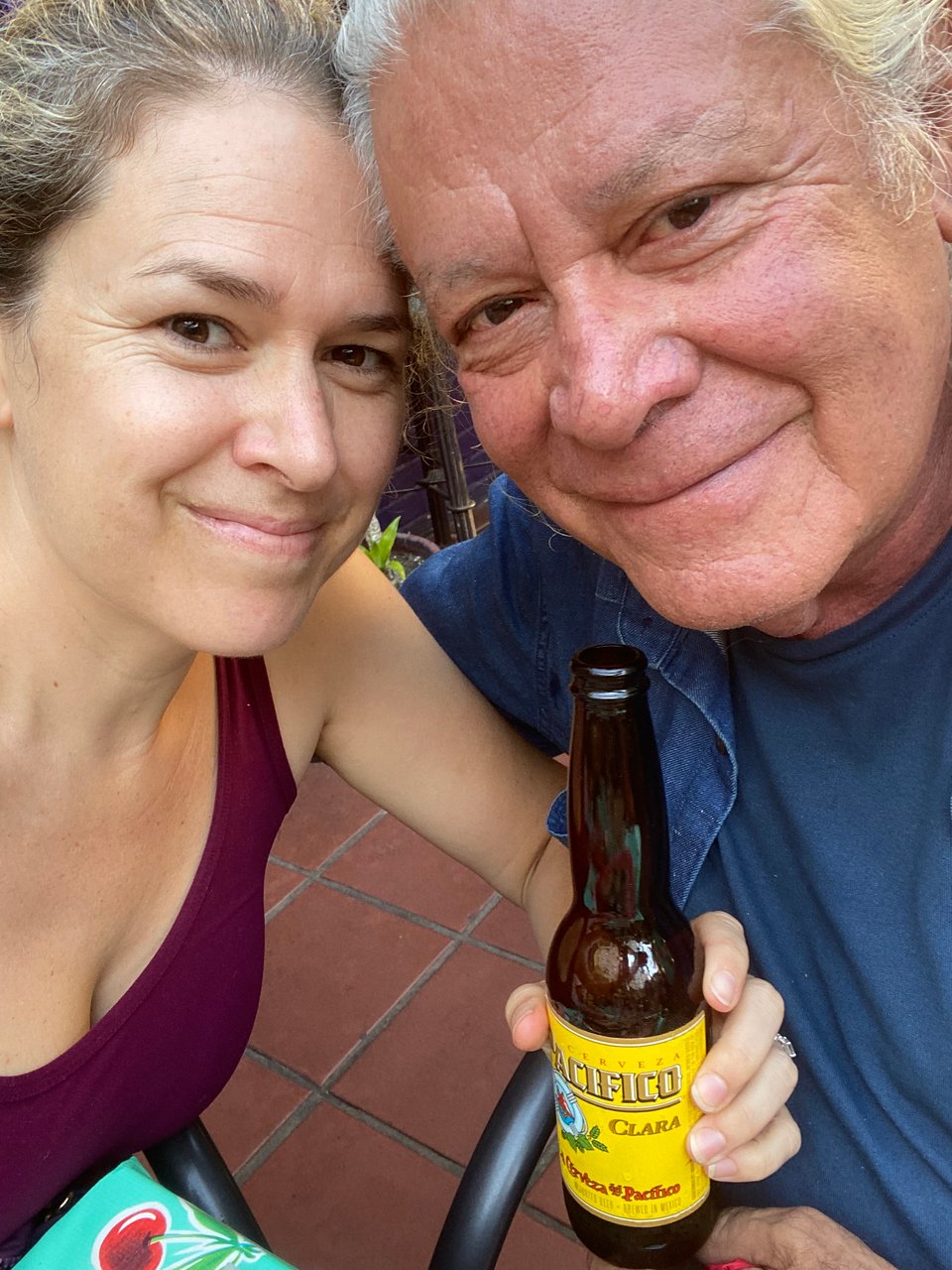 woman posing with older man (her father) while holding bottle of Pacifico Clara beer on outdoor patio