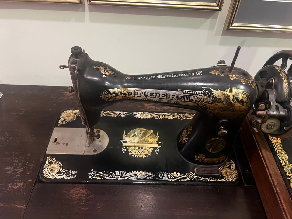 An antique black sewing machine with printed decorations and the brand name Singer in all capital letters in old-fashioned print