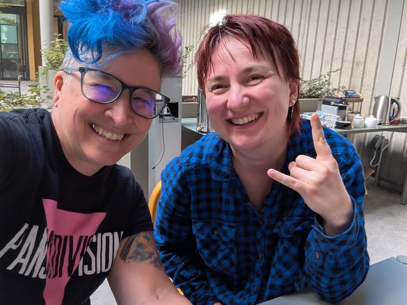 liz and olga smiling on an outdoor patio, liz in Pansy Division tshirt and Olga in a plaid flannel