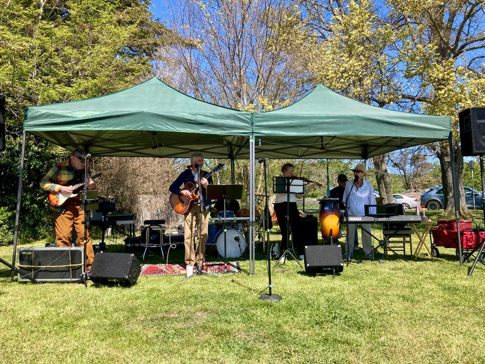 A rock and roll band playing under some tents in a park