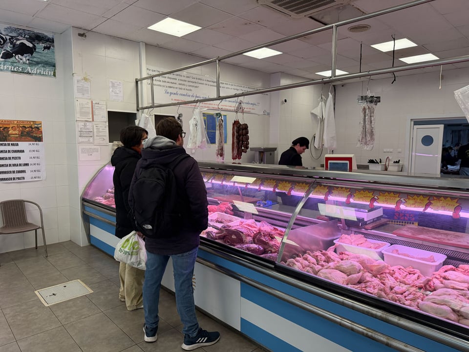 Two people stand at a butcher's counter.