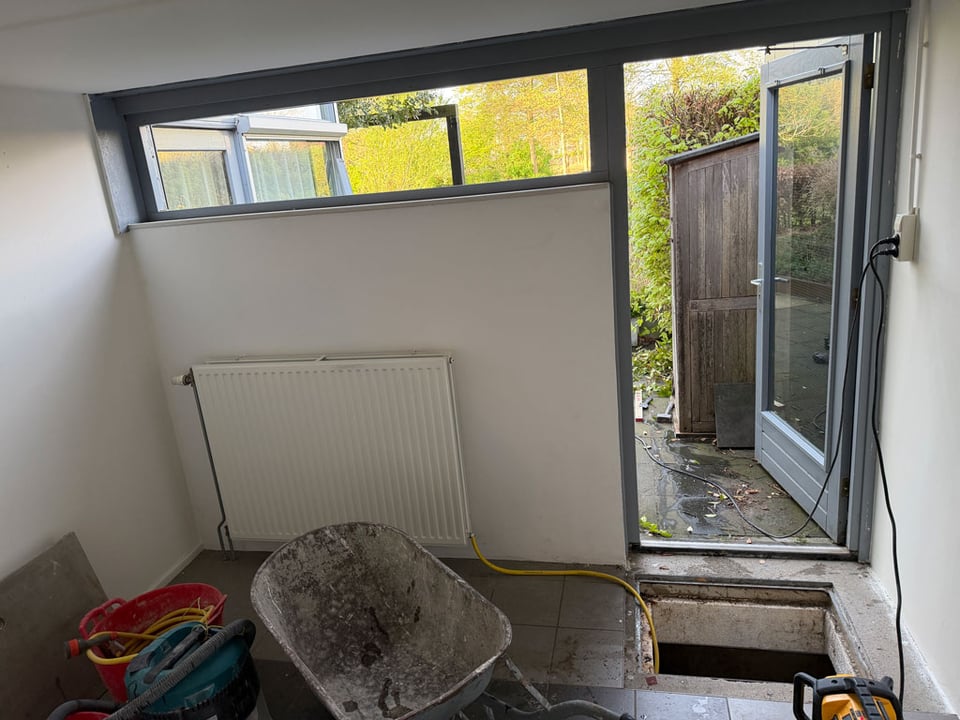 The wall of a room under construction. There are tools and a wheelbarrow. The window is short but long horizontally.