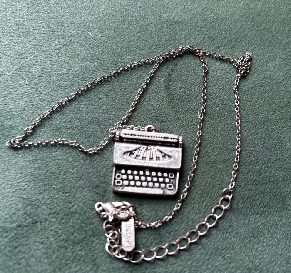 silver chain necklace with typewriter charm on plush seafoam green background