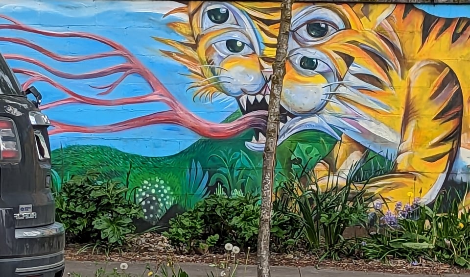A mural with a blue sky over lush greenery. A tiger is stalking thru the greenery except that it has four eyes and a tongue that forks over and over until there are many tongues.