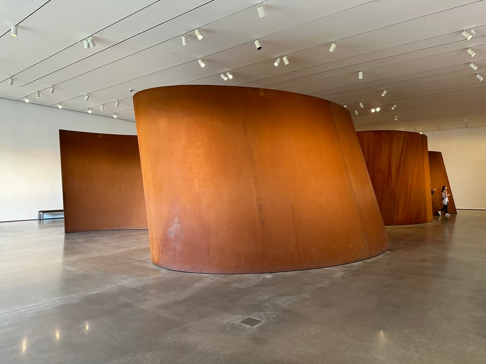 Photo of Richard Serra's curved steel sculpture, BAND. The steel is weathered and brown/orange.
