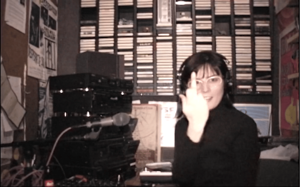 Screenshot of video footage from the 1990s showing a woman giving the middle finger to the camera.