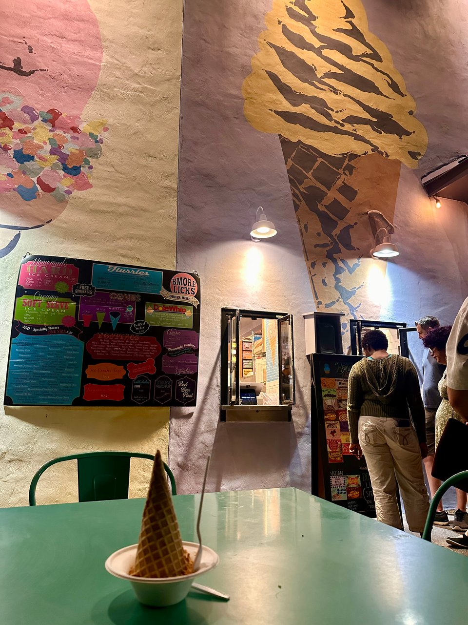 a scoop of pumpkin biscoff ice cream on a green table outside a charming ice cream shop with a takeout window and colorful murals on the walls.