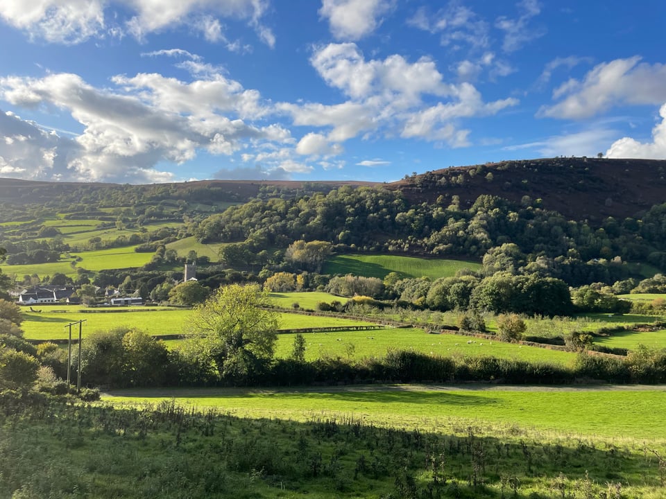 A view of Cwmdu with the church in the distance. Bright blue sky and clouds.