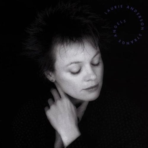 A black and white photo fo Laurie Anderson, a white woman with short spiky dark hair. Her eyes are closed, her head titled at a slight angle to the left, and her hand is gently touching her throat.