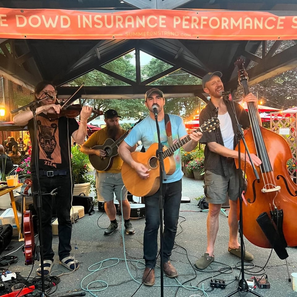 A fiddle player, two guitarists and an upright bassist perform together at a street fair.