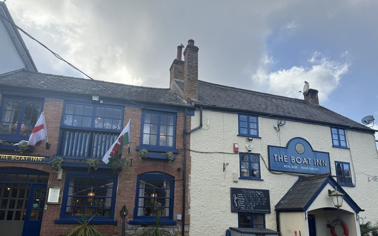 A pub, also called an Inn, a white / plain brick front with navy blue window frames and a lighter blue sign The Boat Inn. Very quaint!