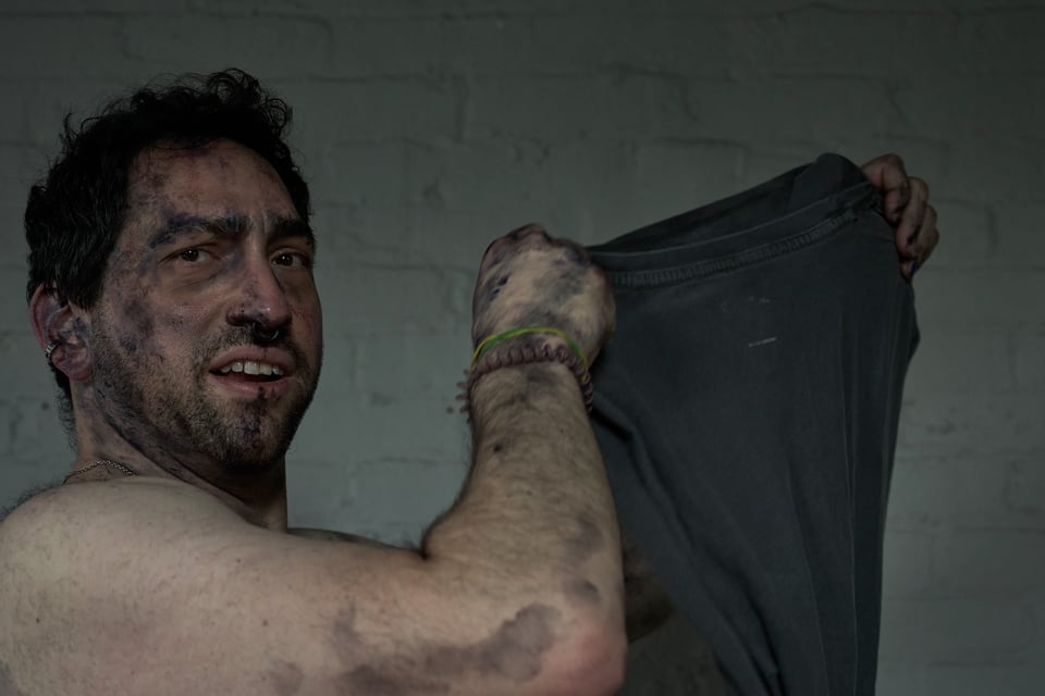 dirty man taking off his teeshirt as he glances at the camera