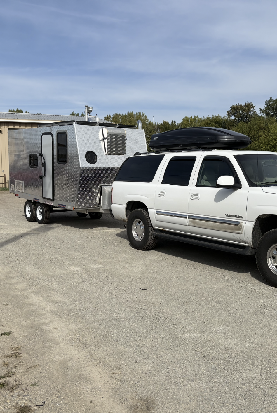 A white SUV pulling a camper trailer, the exterior of which is paneled with diamond plate.