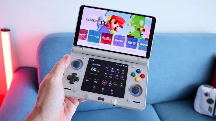 hand holding a dual screen retro gaming handheld in front of a blue couch