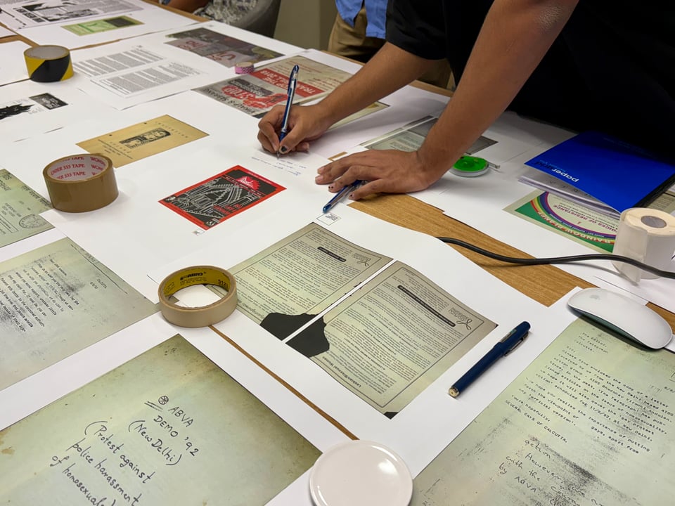 A right-handed annotation of prints on a large white table with various packaging tape rolls serving as paper weights.