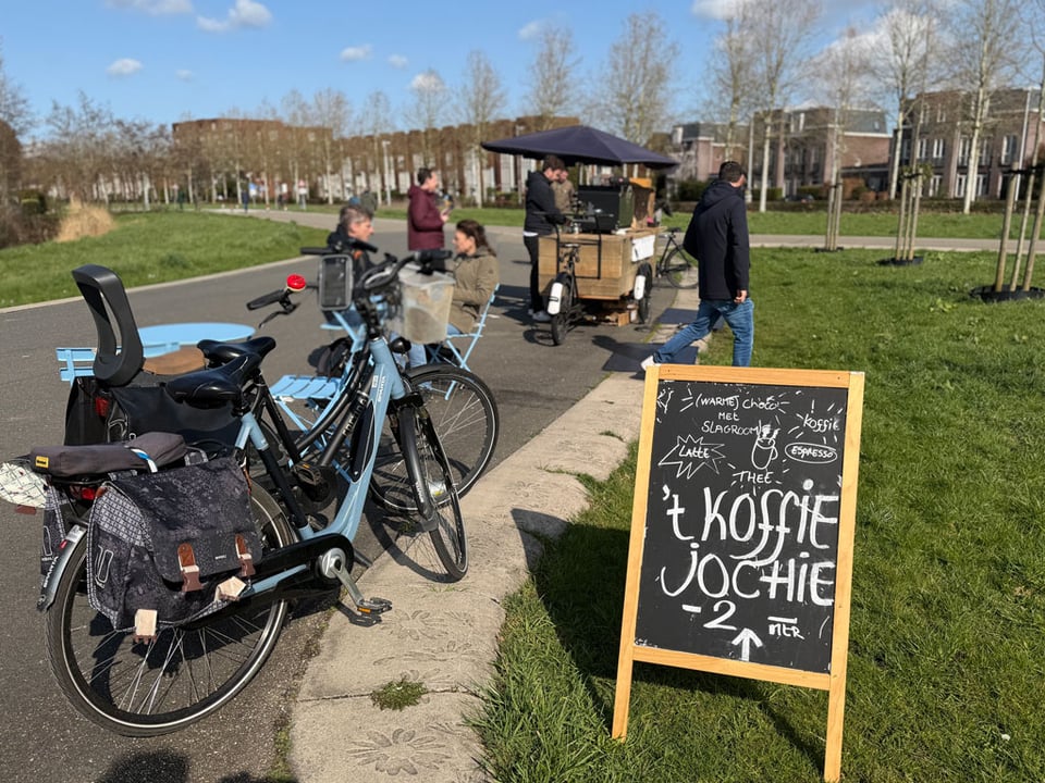 Bikes are parked next to a pop-up coffee stand in a park.