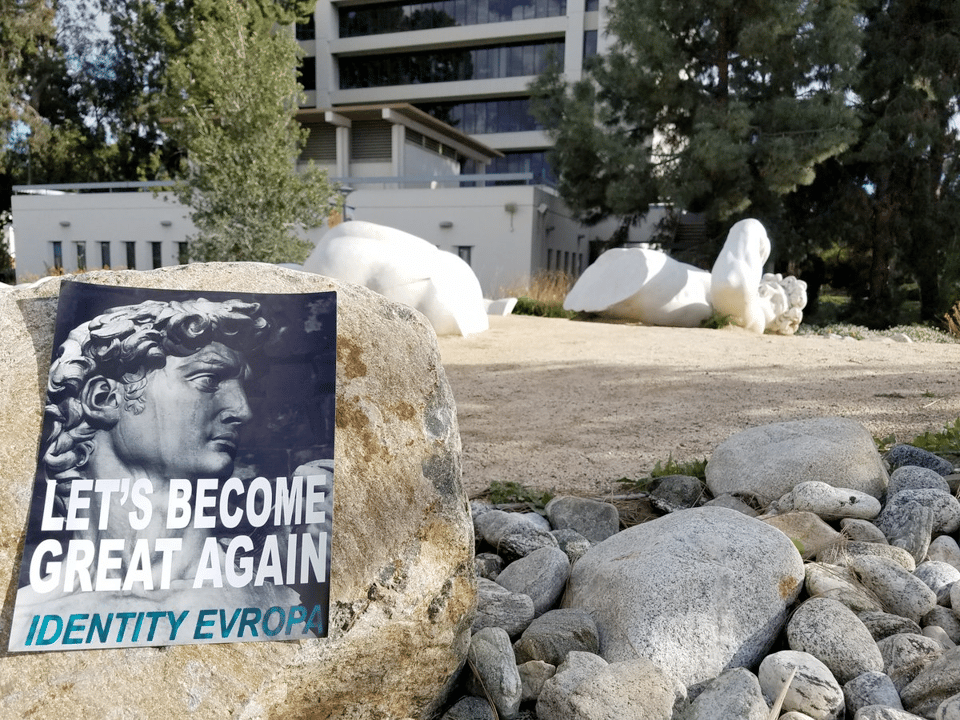 a poster for a white nationalist group on the Cal State Fullerton campus in front of of a fallen replica of a white ancient Greek statue