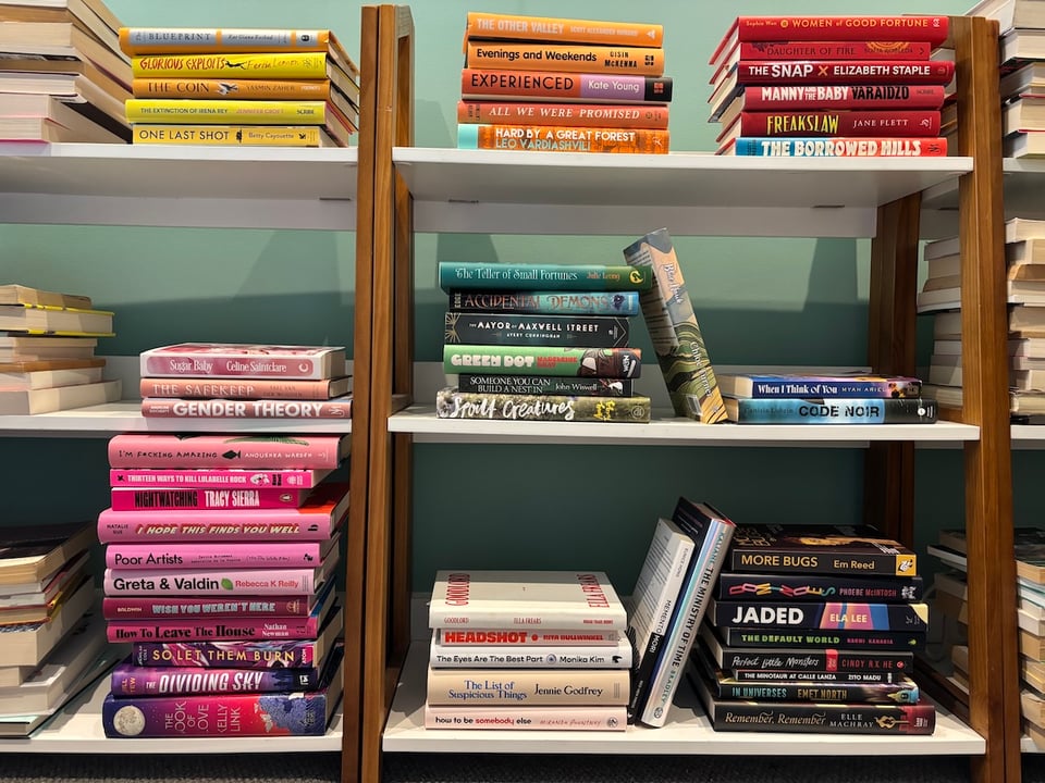 A collection of around 50 novels, mostly hardback, in piles by spine colour. The pink pile is substantially the biggest.