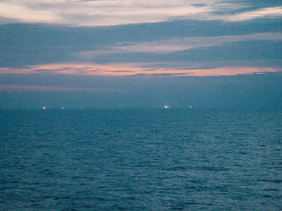 黃昏的海面上雲間有晚霞,海平面上有燈光