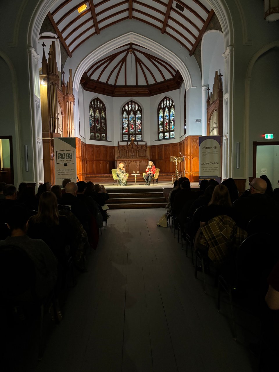 Kate and Amal on stage in front of a crowd in an event space that used to be a church.