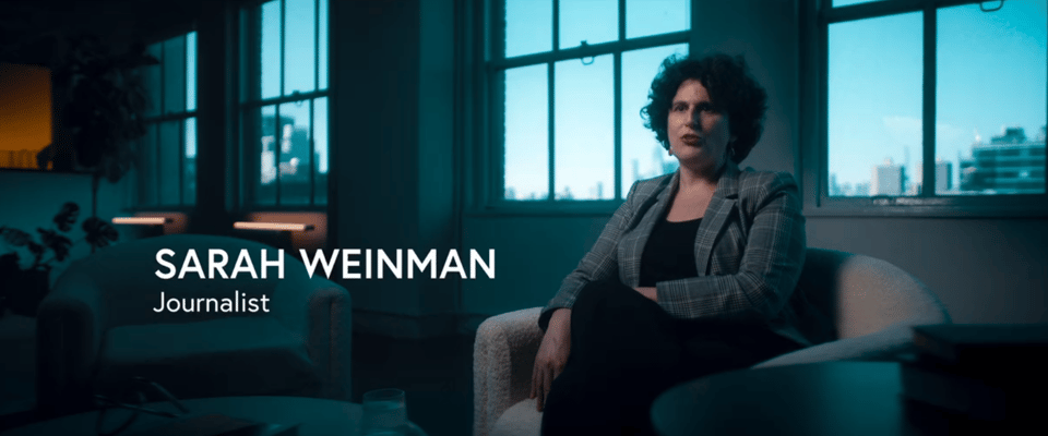 SARAH WEINMAN
Journalist

A woman with dark curly hair in black pants and shirt (covered by a grey blazer) is interviewed for a TV documentary episode