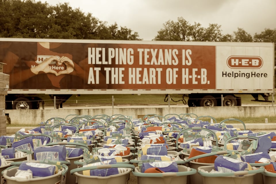 Rows of plastic tubs filled with gloves, paper towels, and disinfectant sit ready in a parking lot—H-E-B’s contribution to flood relief after the deadliest disaster in Texas history over the July 4 weekend. Behind them, a branded semi trailer reads, “HELPING TEXANS IS AT THE HEART OF H-E-B.” When the state fails, the grocery store shows up.