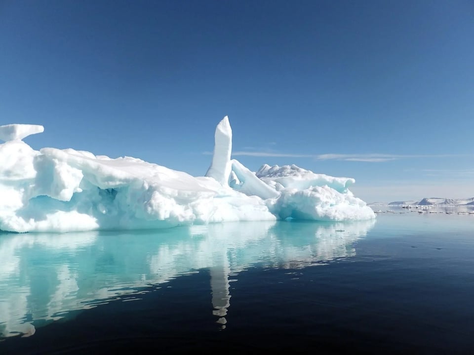 A white stack of pack ice is reflected in the turquoise ocean, against a clear blue sky, near Baffin Island.