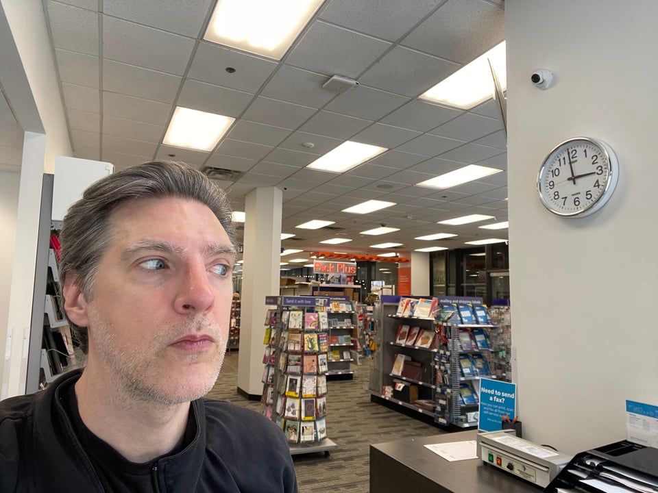 A man looks behind him at a FedEx Office full of business books and harsh lighting