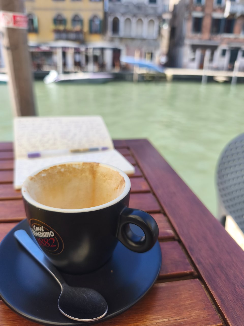 image of an empty cappuccino and a notebook and canal in the background
