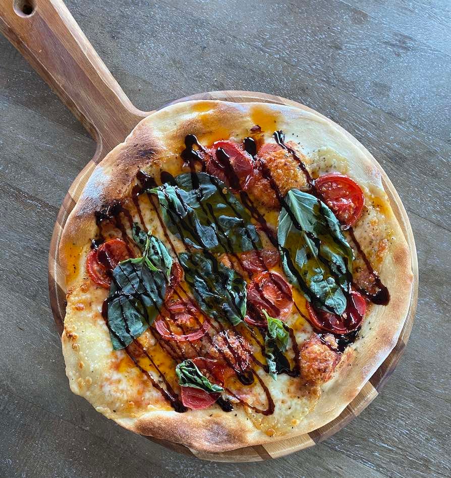 a homemade pizza with tomato, basil, fresh mozzarella and balsamic drizzle