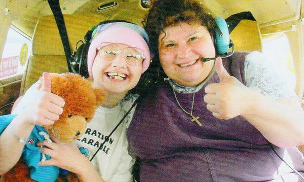 Gypsy Rose Blanchard and her mother Dee Dee, both wearing aviation headsets, give a thumbs-up inside a small aircraft; Gypsy holds a teddy bear.