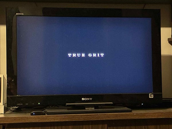 A television with a blank screen and the words True Grit in white letters