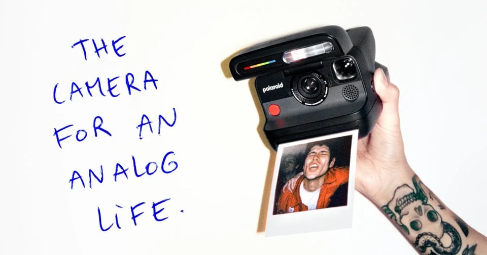 Advert for the Polaroid Flip camera. A handwritten headline reads, "THE CAMERA FOR AN ANALOG LIFE." We see a tattooed forearm and a hand holding a Flip camera, out of which is coming a Polaroid photo of a man with an ecstatic look on his face. It looks like he's on a dancefloor or at a music gig.