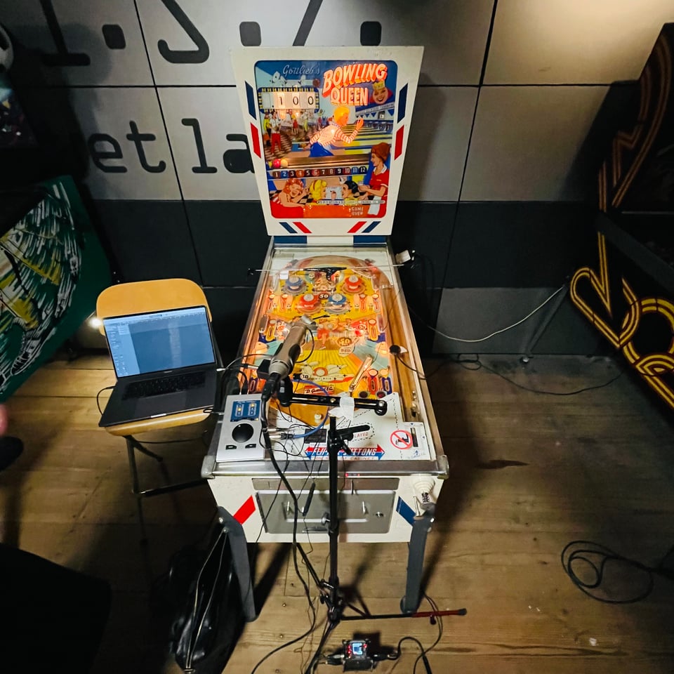 An older pinball machine with sound recording equipment next to it.