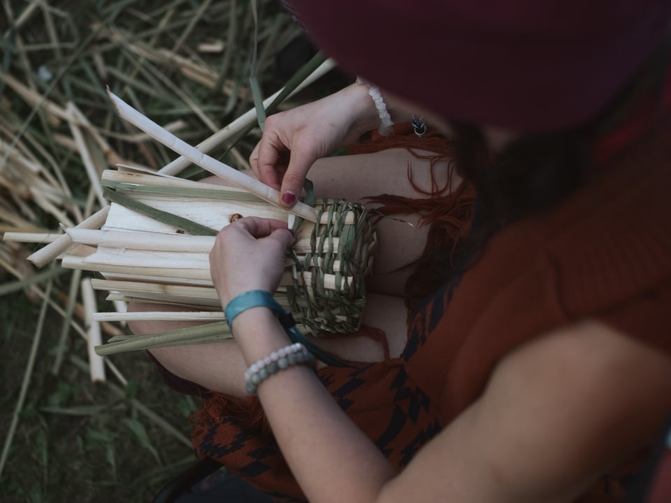 woman weaving a berry basket with cattails