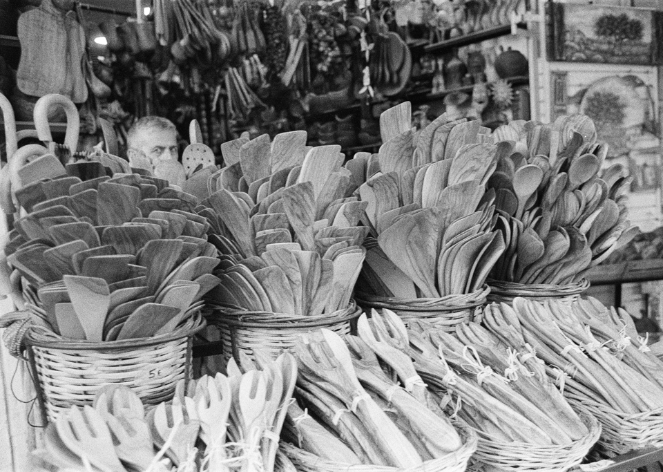 A pile of wooden utensils for sale with the owner peeking out behind them.