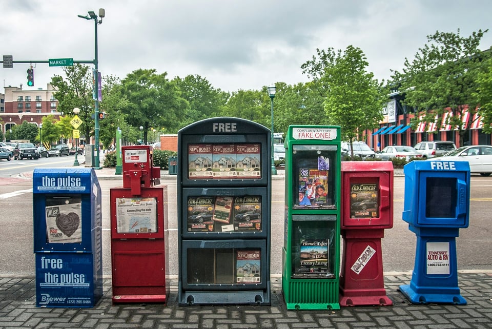 A person, seated, reads a newspaper. Photo by Adi Lica on Unsplash