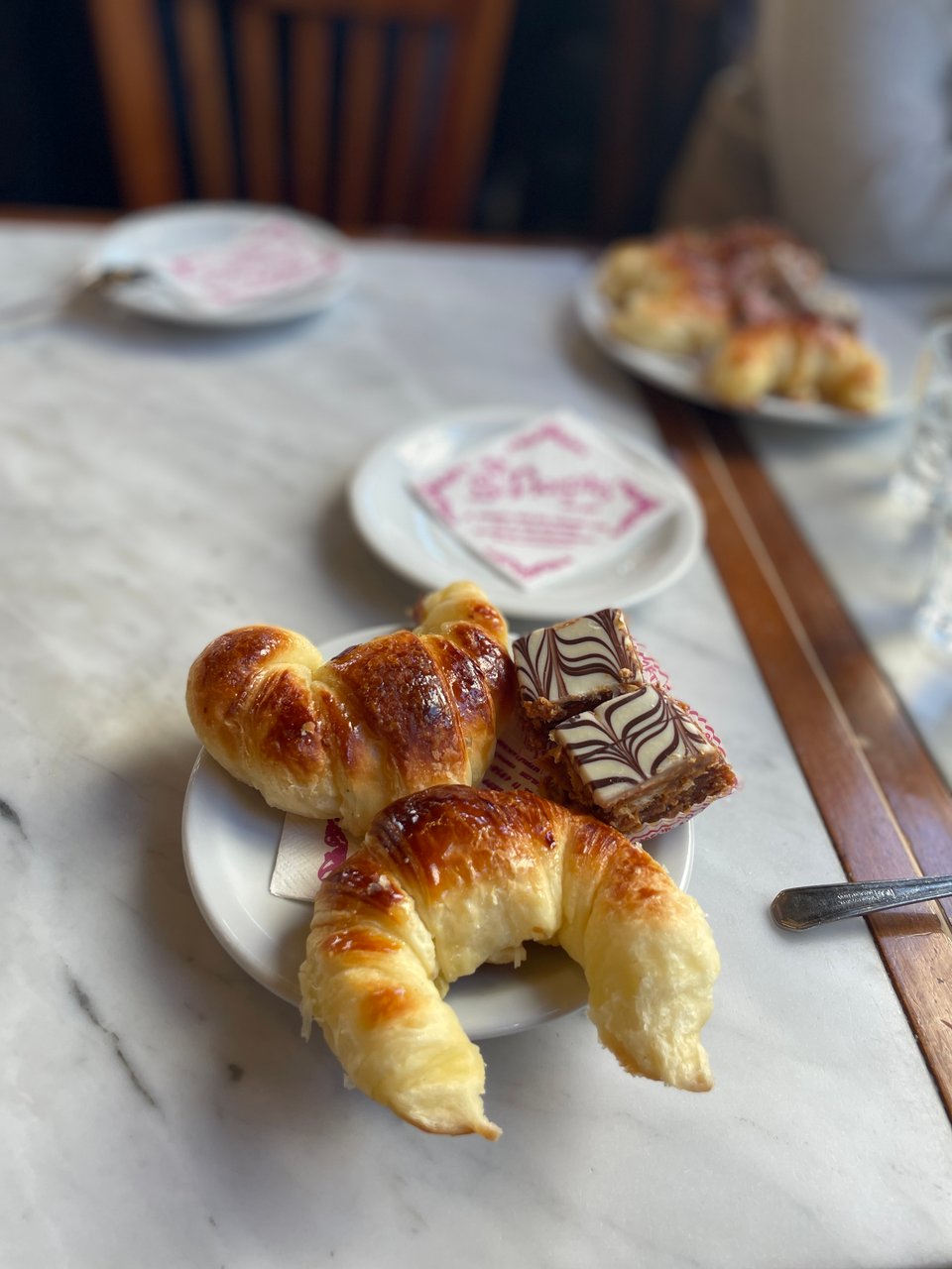 Two sweet medialunas on a plate with two squares of a pastry. The plate is on a marble topped table.