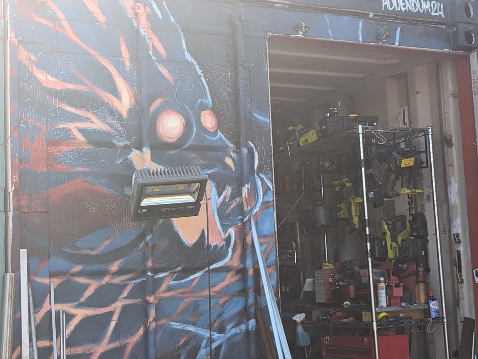 A spooky looking monster lurking on a wall next to a warehouse full of stuff