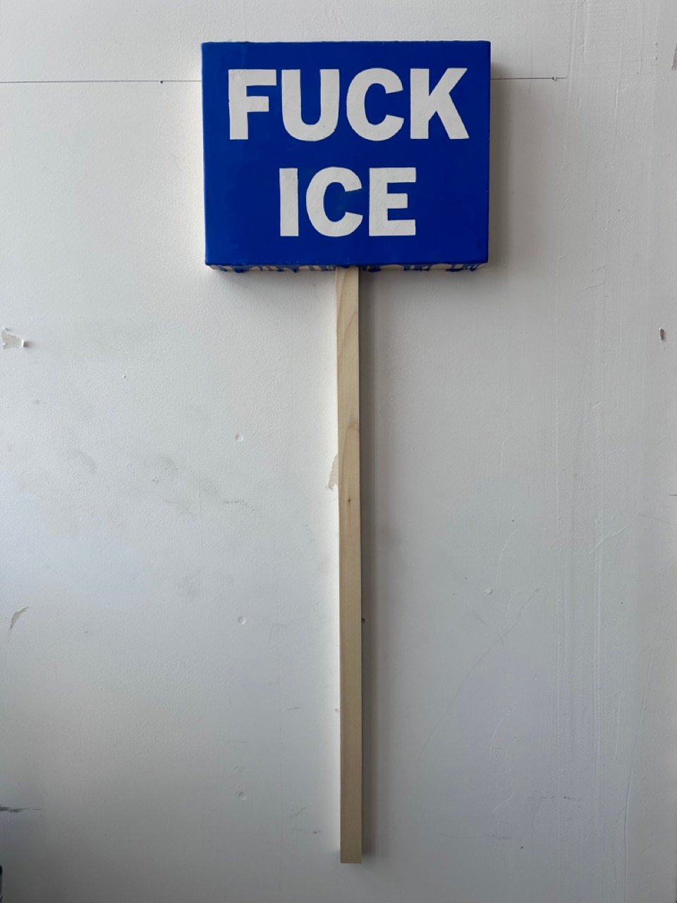 Little blue painting with FUCK ICE in white letters. Stick is attached t make it look like a sign.