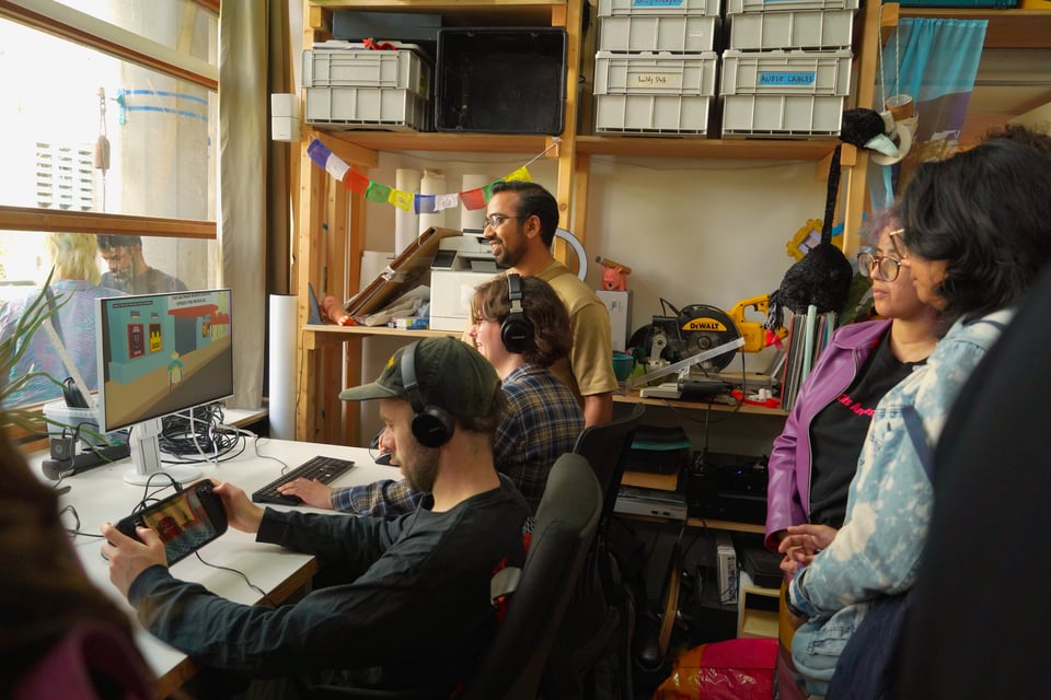A group of people watch a bank of two screens lit up by a videogame.