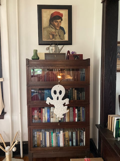 Photo of ghost decoration hanging on barrister bookshelf filled with books.
